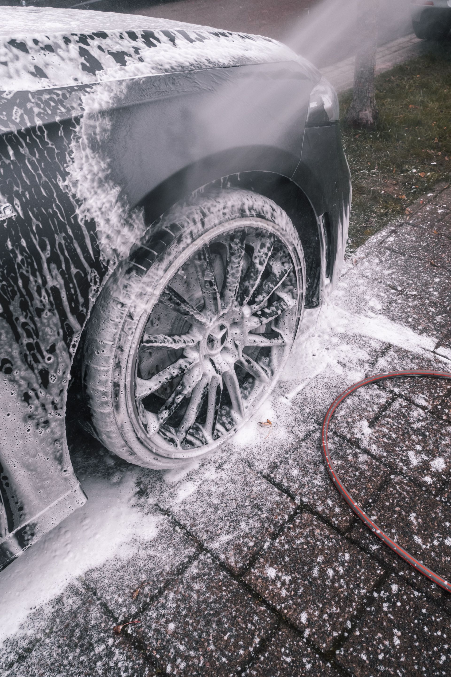 Close-up of a luxury car wheel being thoroughly washed with foam outdoors.